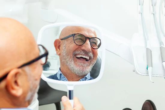 older man smiling in the mirror, looking at his new dental implants
