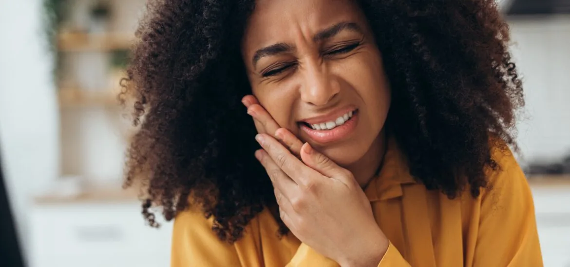 woman in yellow shirt holding her jaw, serious tooth pain