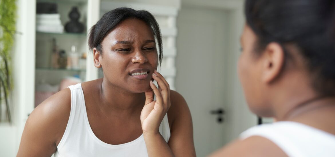 young woman looking in the mirror holding her jaw, night time bruxism