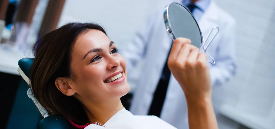 Beautiful young woman looking at mirror with smile in dentist’s office