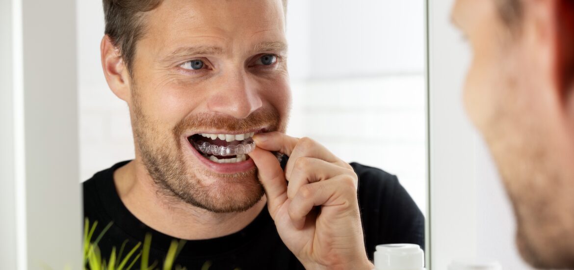 adult man looking in mirror and inserting Invisalign clear aligners