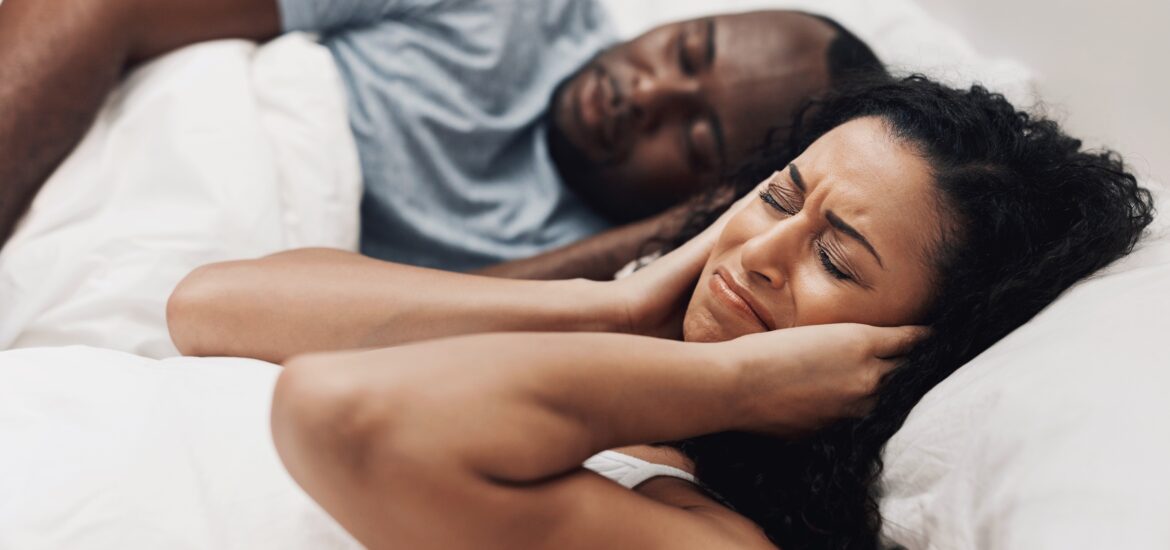 woman covering her ears in bed white her partner snores