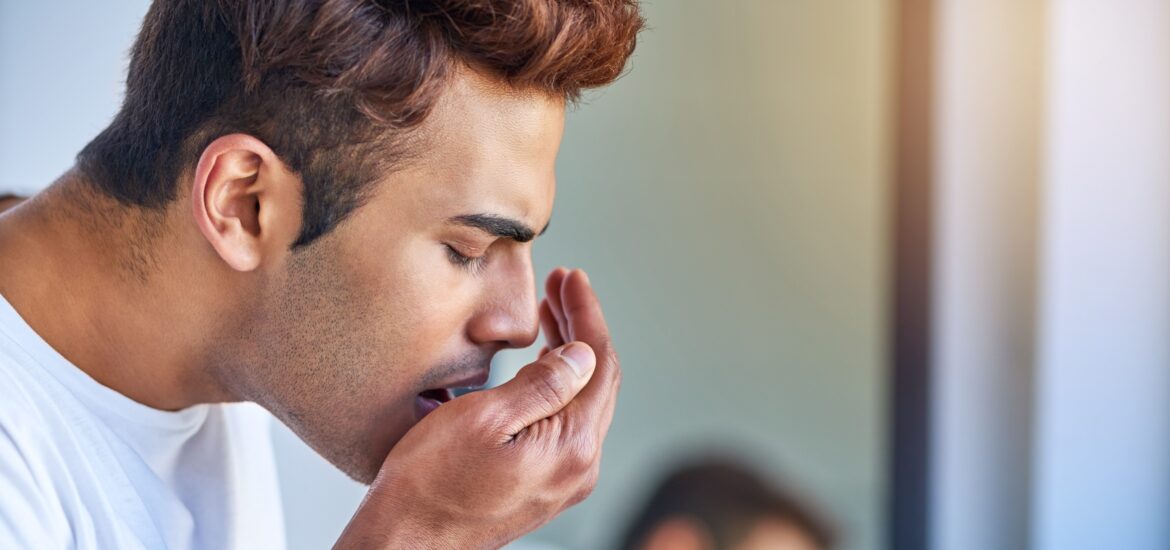 young man blowing on his hand checking his breath in the mirror